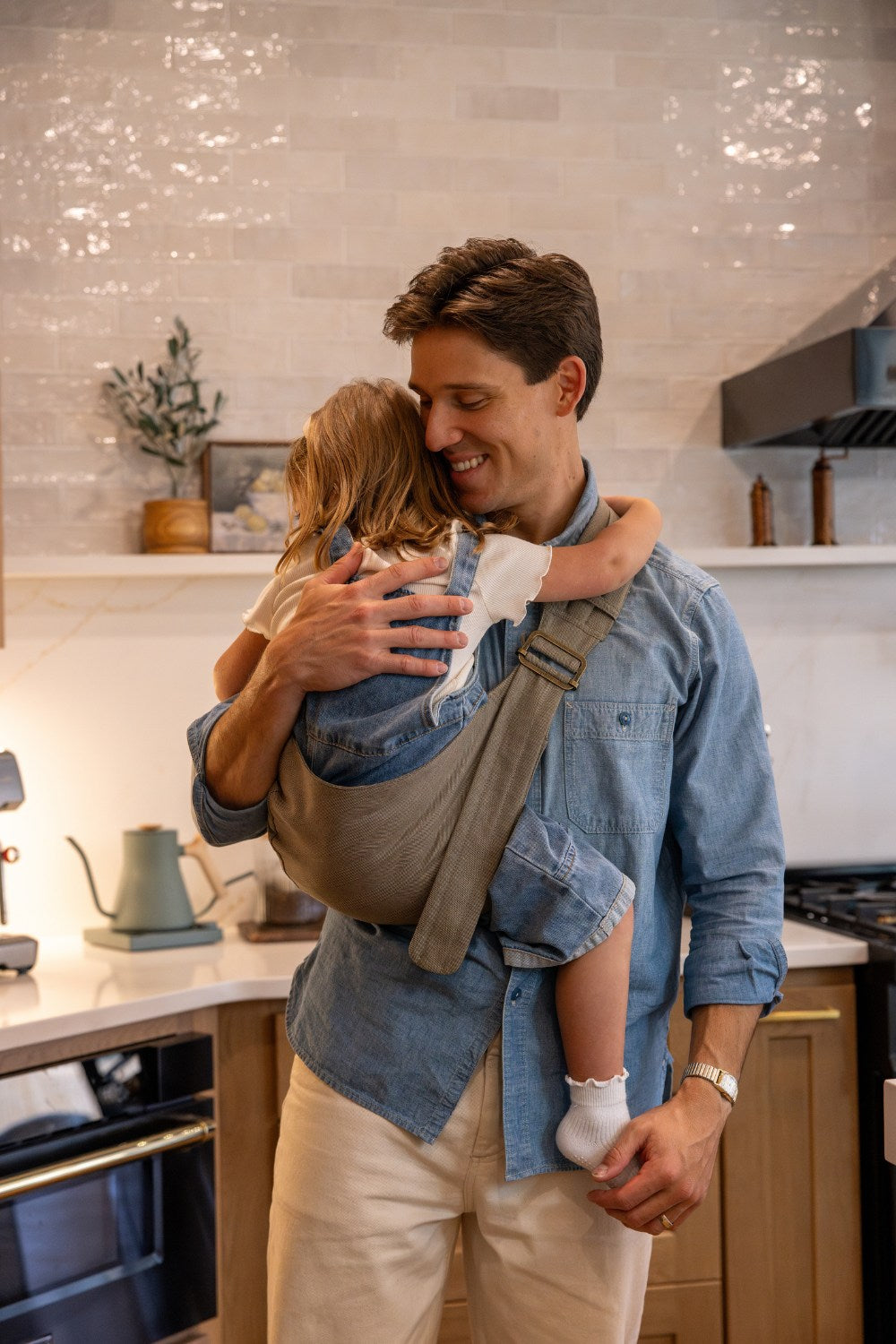 Zach Webber wearing the Mabē Monarch Toddler Sling in Charles Herringbone—which is a delicate herringbone weave cotton/linen fabric in shades of brown—with a toddler girl.