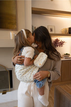 The Mabē Monarch Toddler Sling in Sunday Floral with matching Accessory Bag featuring white cotton/linen fabric with tiny sprigs of blue flowers, worn by Liz Webber and an older toddler girl.
