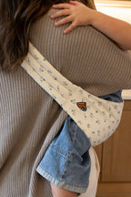 Unseen adult and toddler using a Mabē Monarch Toddler Sling in Sunday Floral, which is solid white cotton/linen with tiny sprigs of blue flowers.