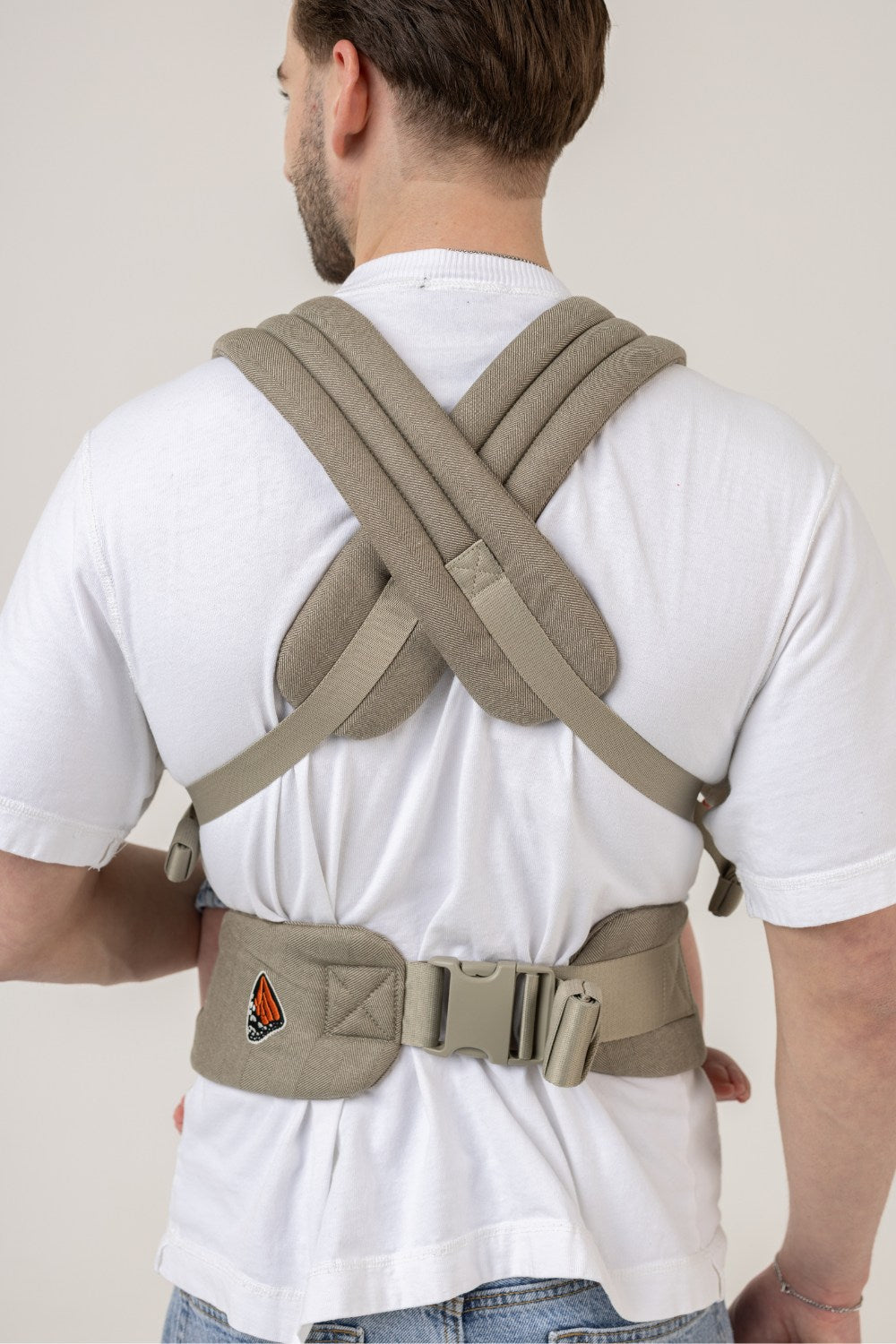 Back view of a man wearing the Mabē Monarch Buckle Carrier in Charles Herringbone, which is a delicate herringbone weave cotton/linen fabric in shades of brown.
