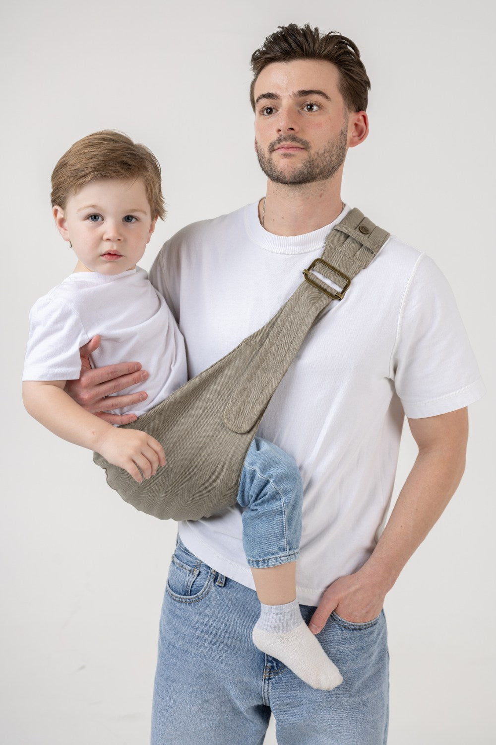 The Mabē Monarch Toddler Sling in Charles Herringbone, which has a delicate herringbone weave cotton/linen fabric in shades of brown, worn by a man with a toddler.