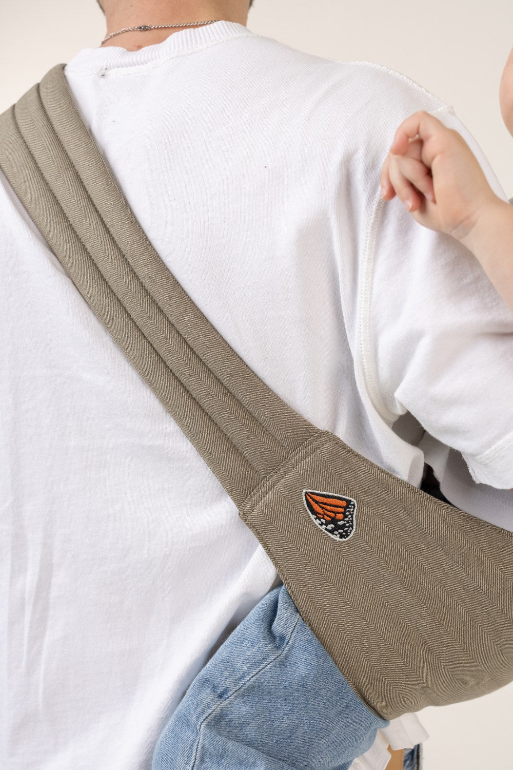 Unseen child in the Mabē Monarch Toddler Sling in Charles Herringbone, which is a delicate herringbone weave in shades of brown, worn by an unseen adult.