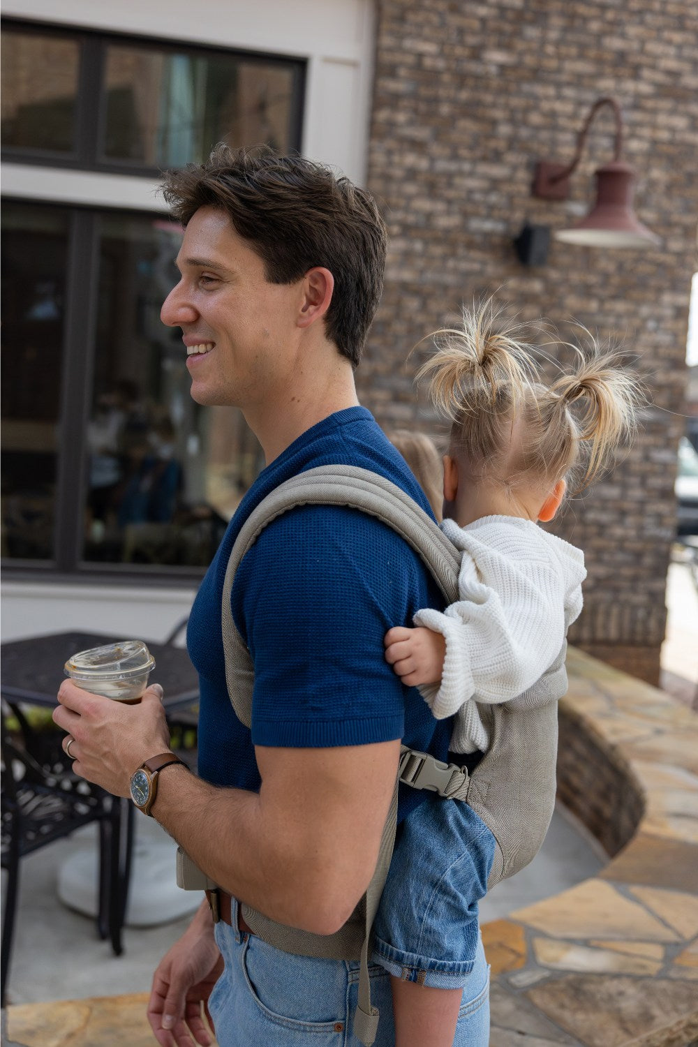 Zach Webber wearing the Mabē Monarch Buckle Carrier in Charles Herringbone, which is a delicate herringbone weave cotton/linen fabric in shades of brown, with a younger toddler.