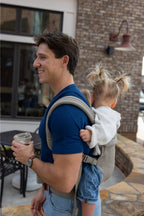 Zach Webber wearing the Mabē Monarch Buckle Carrier in Charles Herringbone, which is a delicate herringbone weave cotton/linen fabric in shades of brown, with a younger toddler.