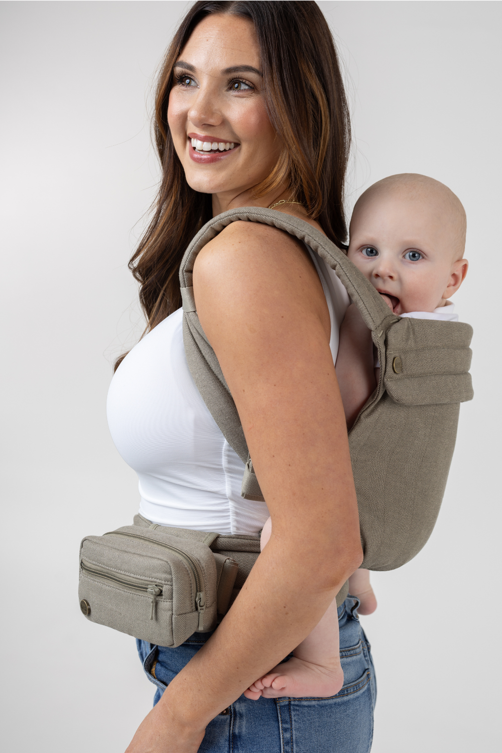 Woman wearing the Mabē Monarch Buckle Carrier and Accessory Bag in Charles Herringbone—delicate herringbone weave cotton/linen fabric in shades of brown—to carry a baby on her back.
