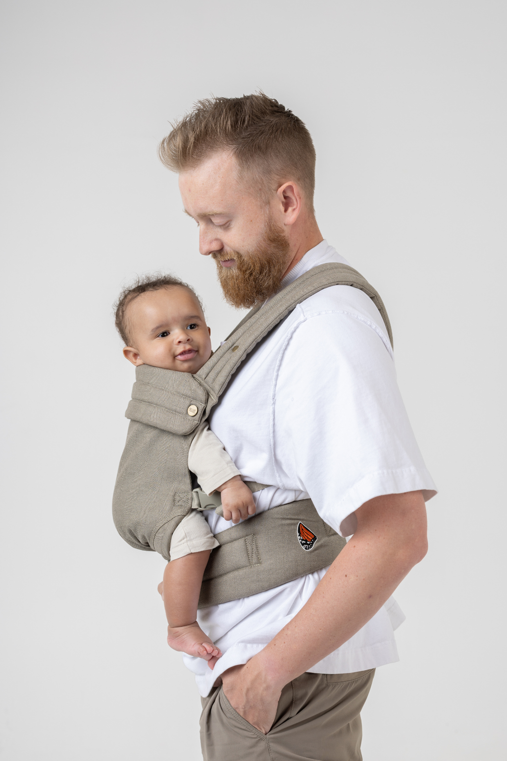 Man wearing the Mabē Monarch Buckle Carrier in Charles Herringbone—a delicate herringbone weave in shades of brown—to carry a baby.