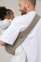 Man wearing the Mabē Monarch Toddler Sling in Charles Herringbone—delicate herringbone weave cotton/linen fabric in shades of brown—to carry a toddler girl.