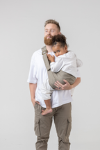 Man wearing the Mabē Monarch Toddler Sling in Charles Herringbone—delicate herringbone weave cotton/linen fabric in shades of brown—to carry a toddler girl.