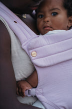 Close-up of a baby looking out from the Mabē Monarch Baby Carrier in Lilac Skies, a soft light purple.