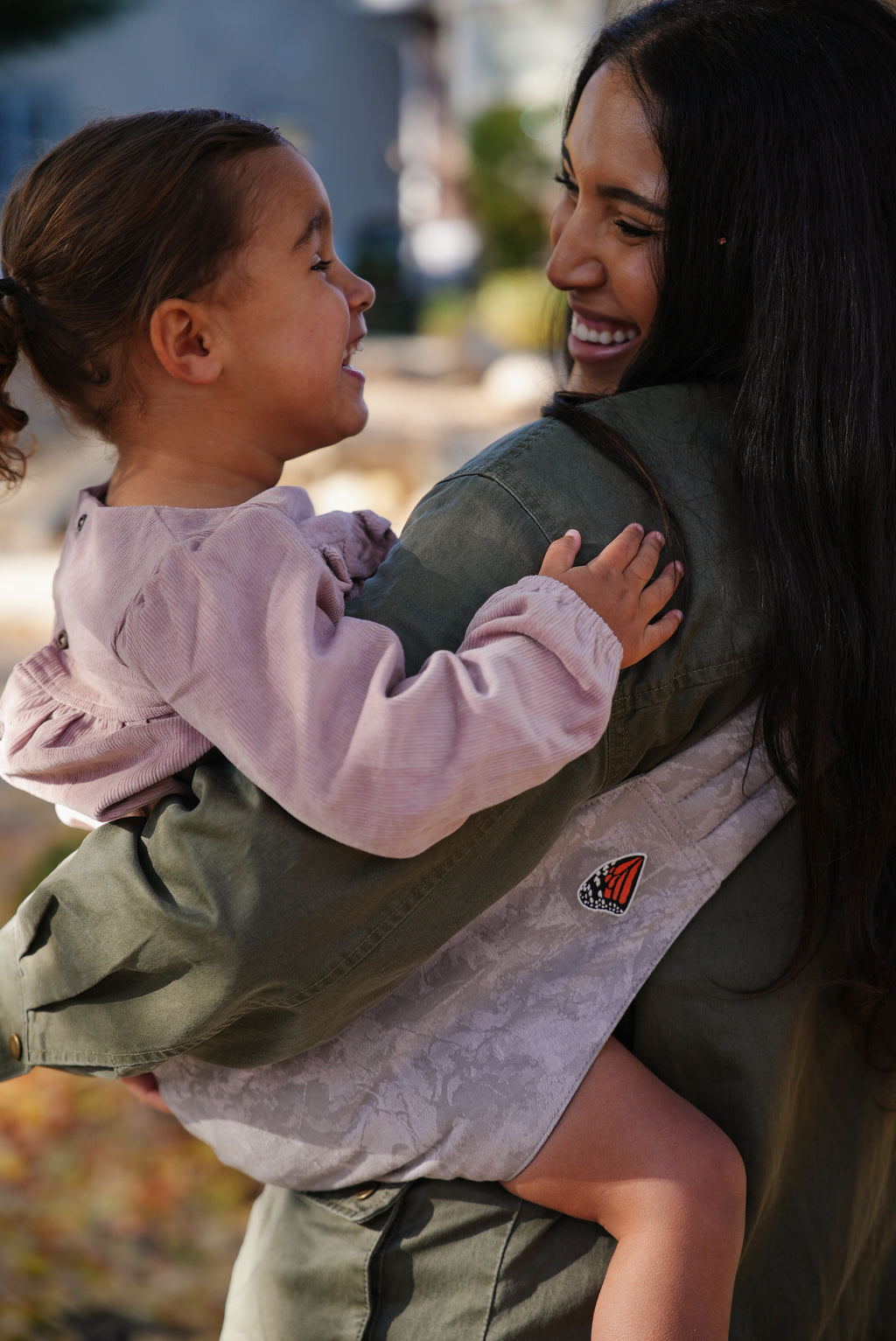 A mom laughs with her toddler on her hip in the Mabē Monarch Toddler Sling in Ashland Camo.