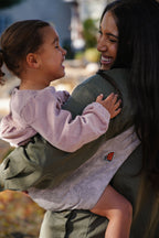 A mom laughs with her toddler on her hip in the Mabē Monarch Toddler Sling in Ashland Camo.