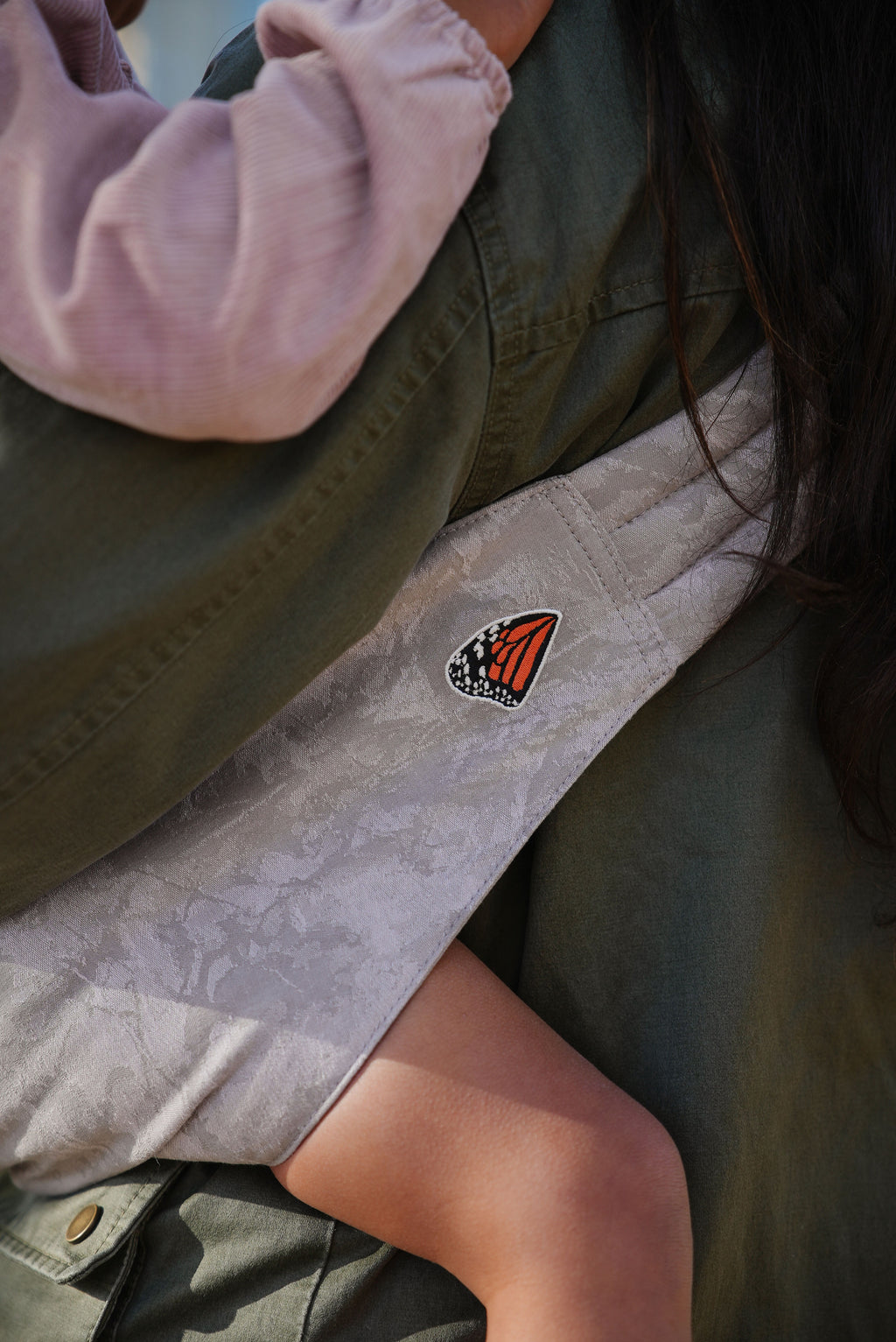 Close-up of the Mabē Monarch Toddler Sling in Ashland Camo, showing the light gray camo fabric and butterfly logo patch.