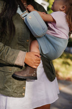 Close-up of a toddler on mom's hip in the Mabē Monarch Toddler Sling in Dream Wash Denim, with a matching denim accessory bag.