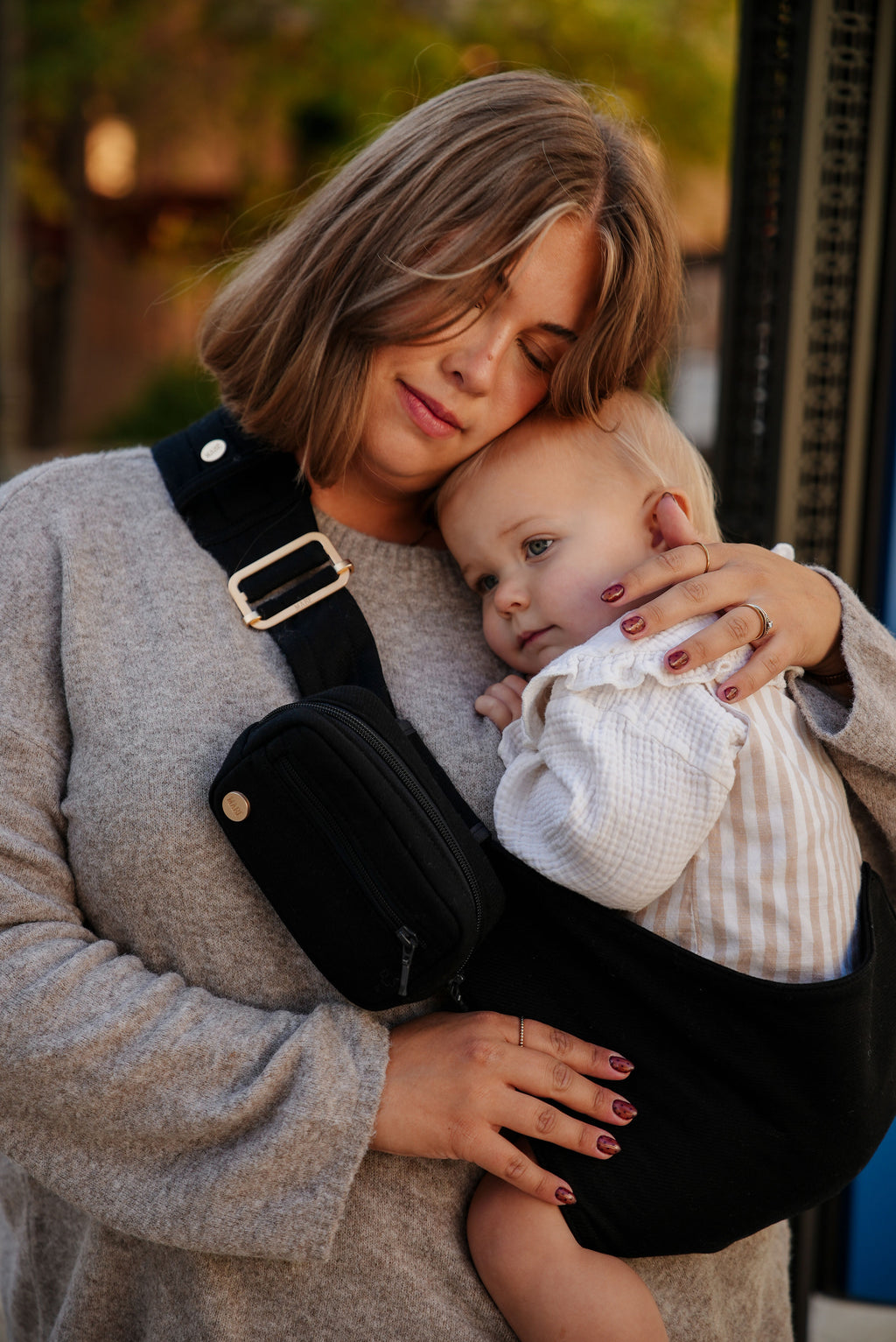 A mom cuddles her toddler on her hip in the Mabē Monarch Toddler Sling in Ebony.