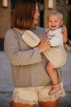 A smiling mom carries her toddler on her hip in the Mabē Monarch Toddler Sling in Houndstooth, with a matching accessory bag on the strap.