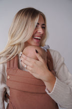 A smiling mom cradles her baby in the Mabē Monarch Baby Carrier in Mocha, close-up.