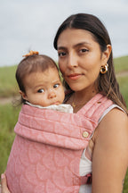A mom holds her baby close in the Mabē Monarch Baby Carrier in Mauve Wings, close-up of the blush pink butterfly print.