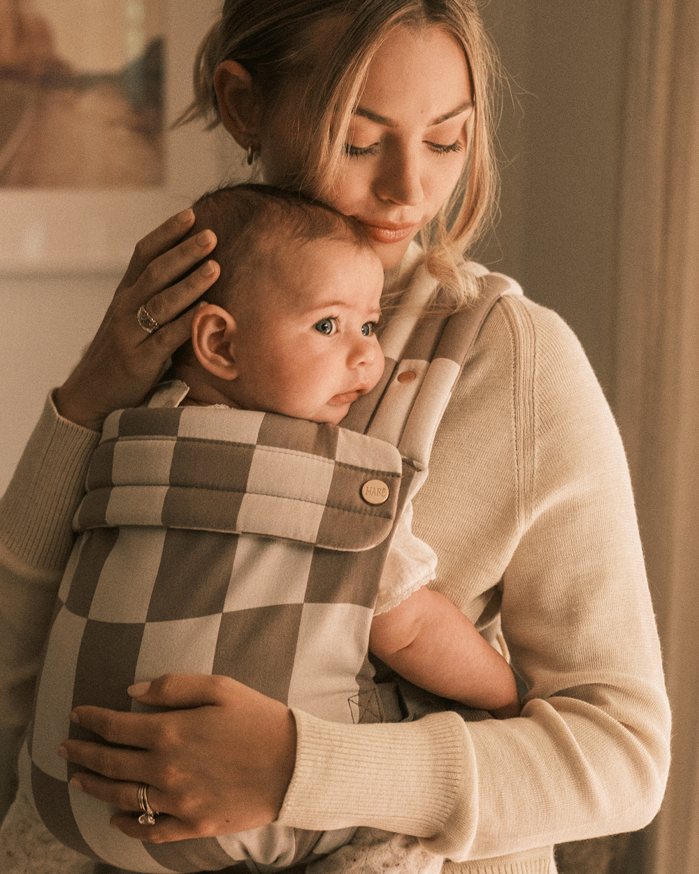 Moving carousel of images showing people wearing small children in the Mabē Monarch Buckle Carrier and Toddler Sling in Wildcard and Spotted Jag (both in Dune colorway).