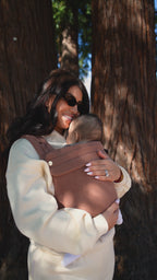 Video of a mom wearing her baby in the Mabē Monarch Baby Carrier in Mocha among tall trees.