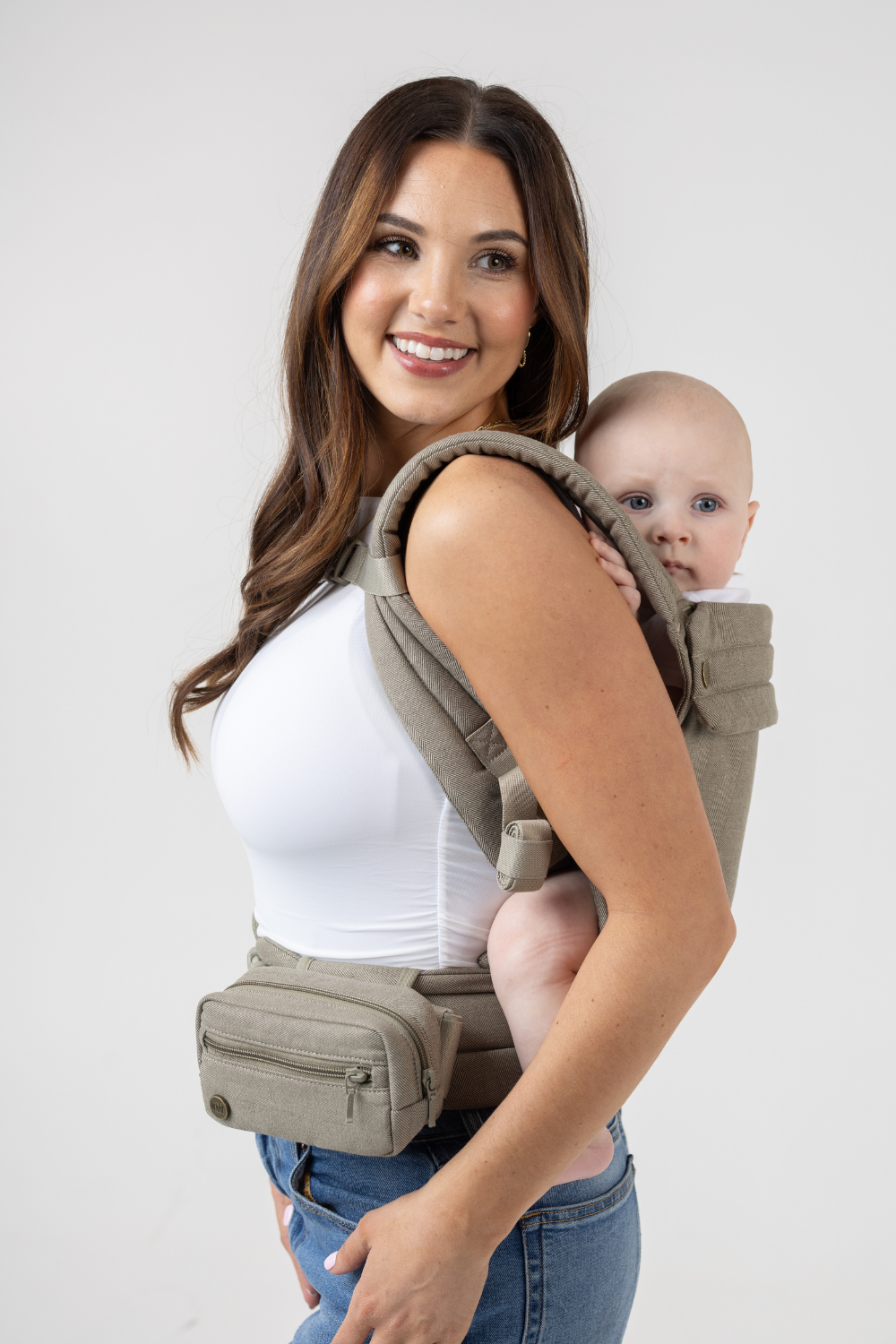 Woman wearing the Mabē Monarch Buckle Carrier and Accessory Bag in Charles Herringbone—delicate herringbone weave cotton/linen fabric in shades of brown—to carry a baby on her back.