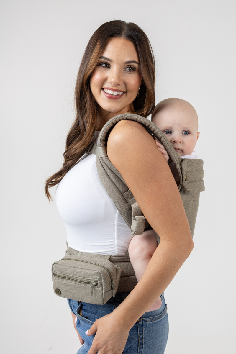 Woman wearing the Mabē Monarch Buckle Carrier and Accessory Bag in Charles Herringbone—delicate herringbone weave cotton/linen fabric in shades of brown—to carry a baby on her back.