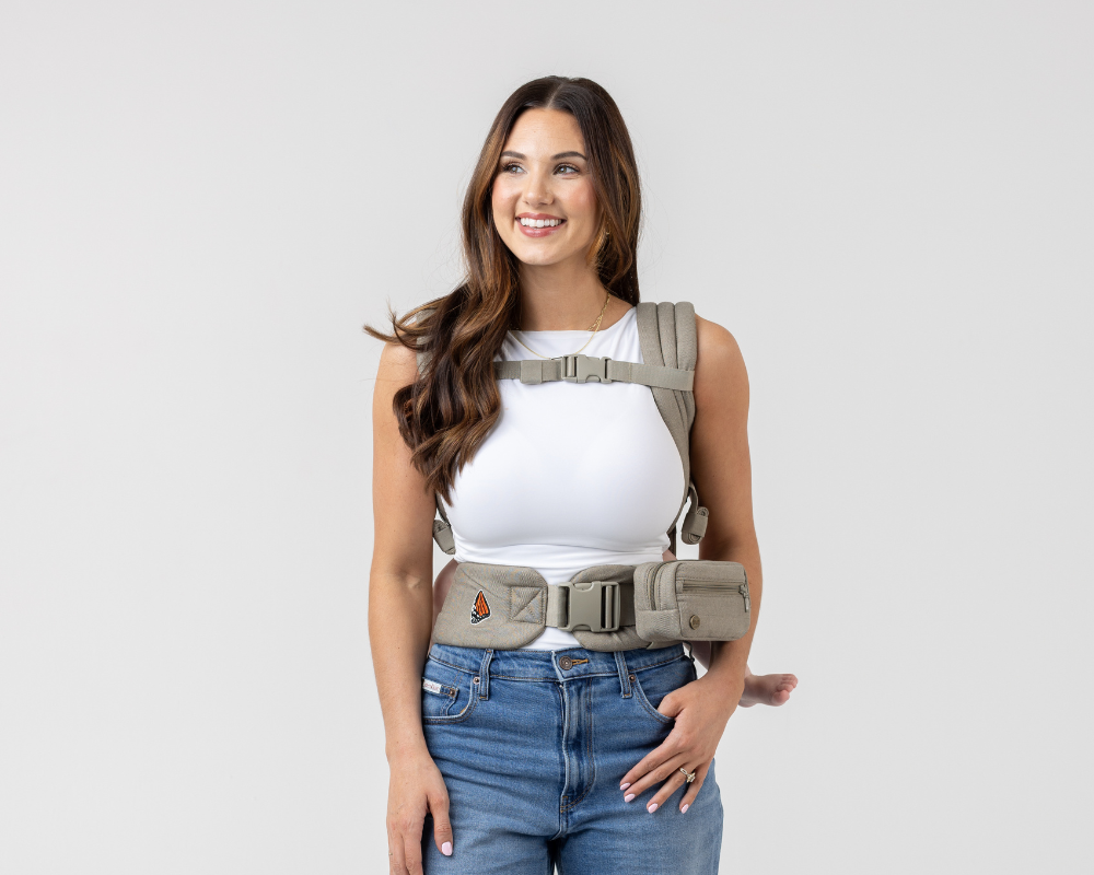 Woman wearing the Mabē Monarch Buckle Carrier and Accessory Bag in Charles Herringbone—delicate herringbone weave cotton/linen fabric in shades of brown—to carry a baby on her back.