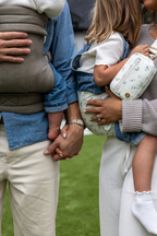 The Mabē Monarch Toddler Sling in Sunday Floral (solid white with tiny sprigs of blue flowers) and Mabē Monarch Buckle Carrier in Charles Herringbone (delicate herringbone pattern in shades of brown) worn by Liz and Zach Webber with their two children.