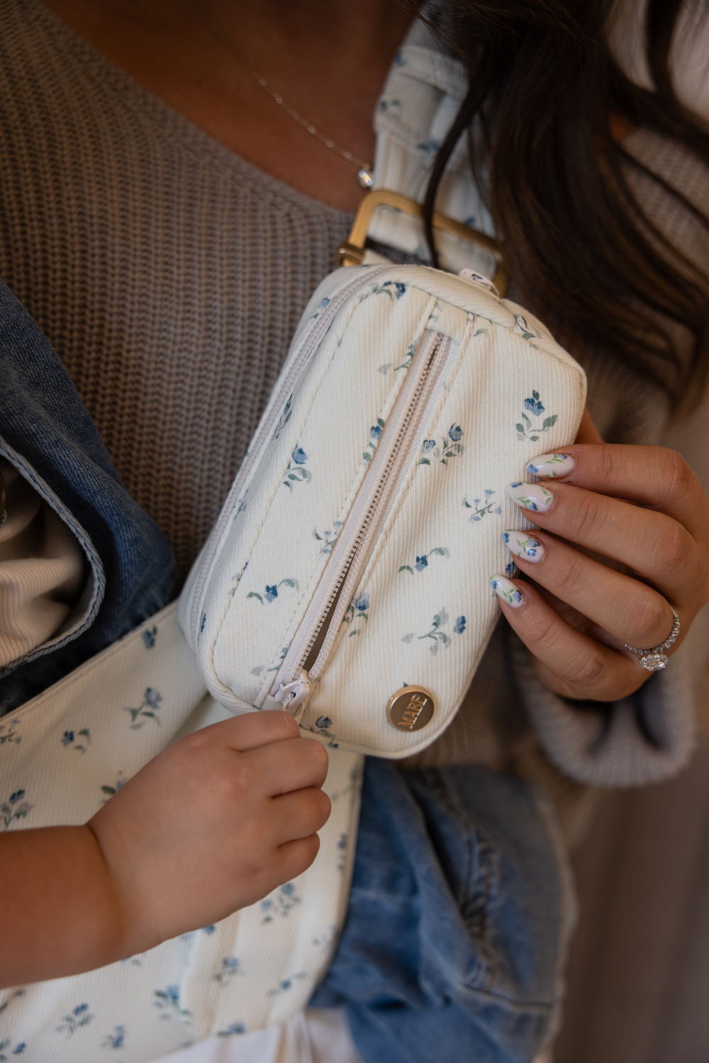 The Mabē Monarch Toddler Sling and Accessory Bag in Sunday Floral, which is white cotton/linen fabric with tiny sprigs of blue flowers.